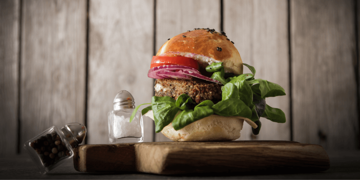 chipotle black bean burger featured image. A vegan burger on a wooden cutting board with a salt and pepper shaker.