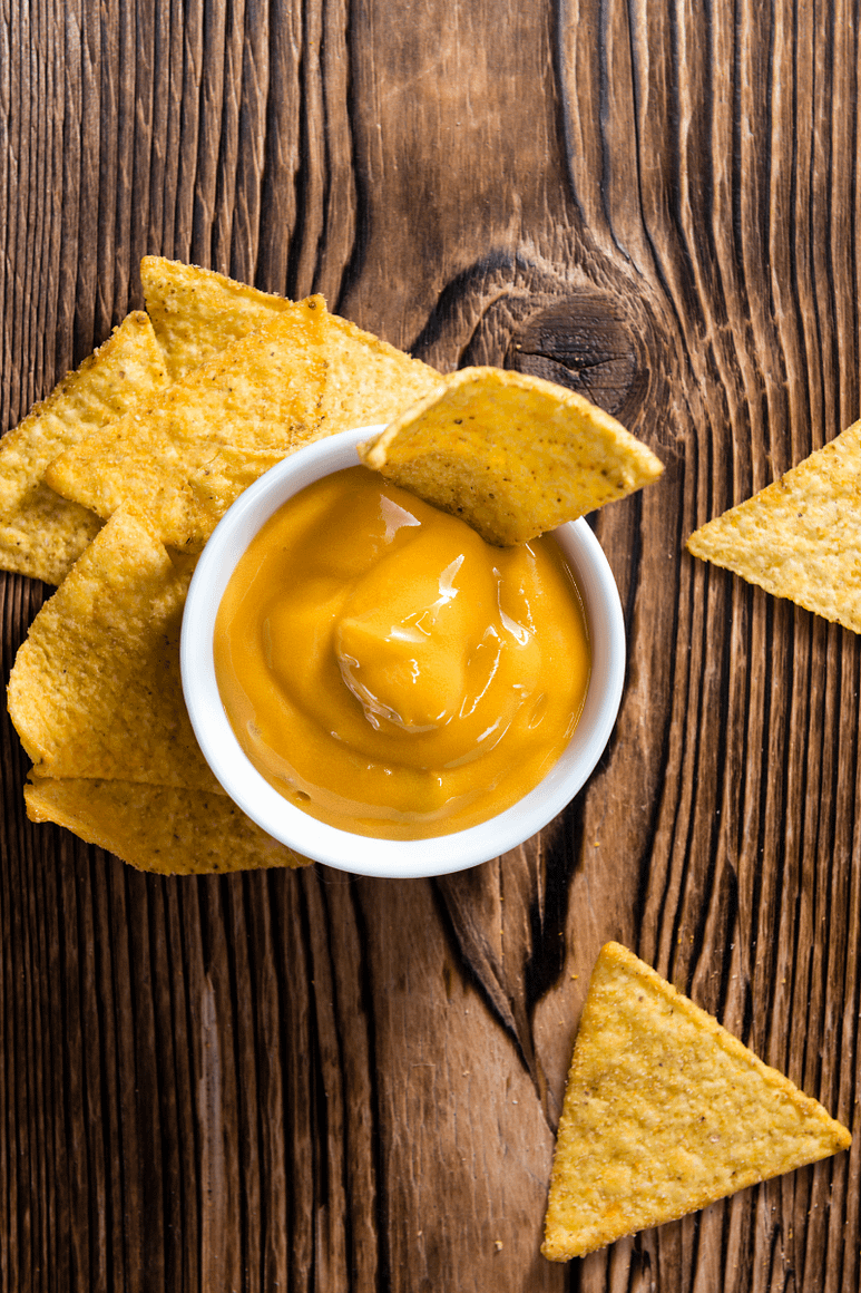 Picture of vegan nacho cheese, vegan nacho cheese recipe, vegan nacho cheese sauce, dairy free nacho cheese on a wooden table. Chip sticking out of the dip in a ramekin. 
