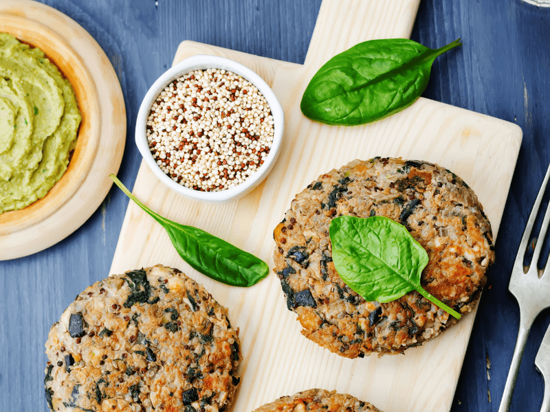 quinoa veggie burgers on a cutting board with spinach and dried quinoa. 